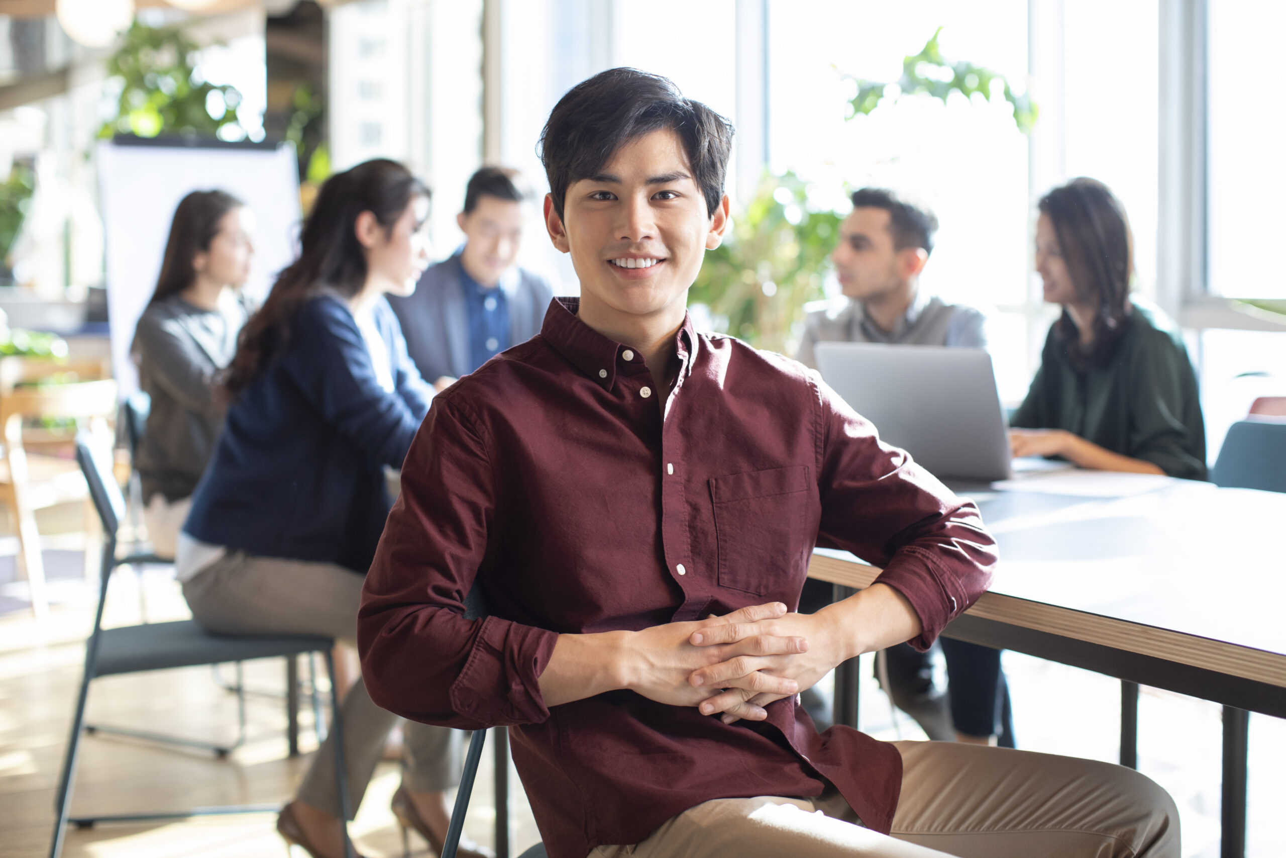A young business intern looking confident while his team is meeting in the background